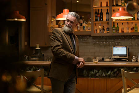 Lonely solid gray-haired adult man drinking whiskey alone at the barの写真素材