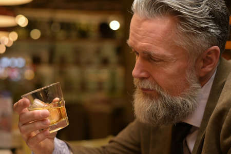 man looks at the whiskey glass in his hand. Adult man drinking in a restaurantの写真素材