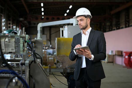 A young plant manager controls the machines process and takes notes on a tabletの写真素材