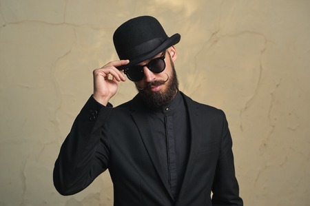 Bearded Man with black Clothes greets. Fashion Portrait
