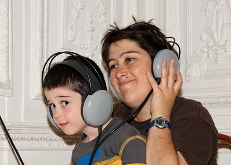 Cute little boy listens to music in earphones with his mother の写真素材