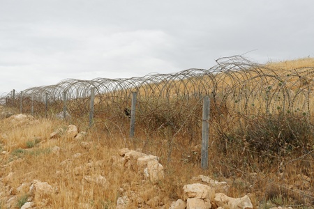 Barbed tape or razor wire fence across the desert hill on cloudy dayの写真素材