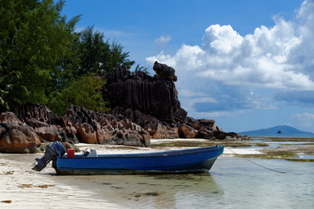 Motor boat at the beach on Curieuse Island, Seychelles, with lava stone rocks and lush vegetationの写真素材
