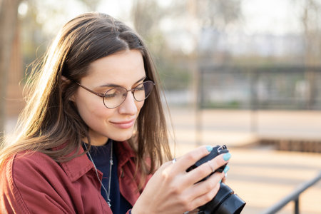 Close up portrait of a charming photographer lady checking settings on her camera wearing eyeglasses...