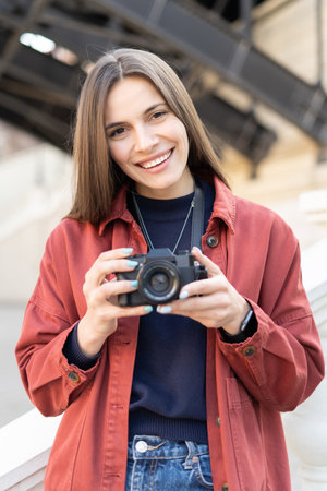 Close up of a smily young photographer holding a mirrorless camera outside while walking in the city, and looking in the cameraの写真素材
