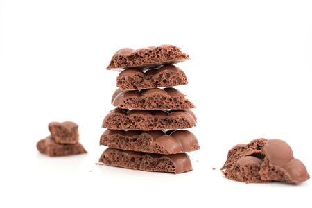 Some pieces of porous chocolate laying on top of each other and one is near on isolated white...