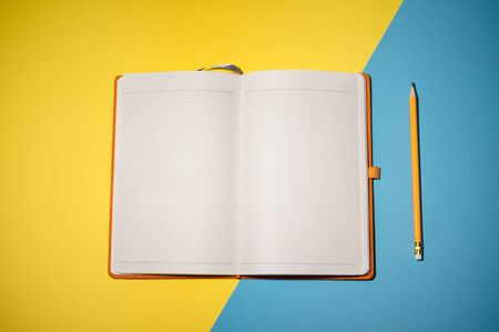 Opened book and pencil on it on the yellow and blue background. Space for text. Top on view.の写真素材