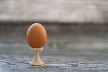 One brown chicken egg standing in holder on the grey wooden background. Space for text.の写真素材