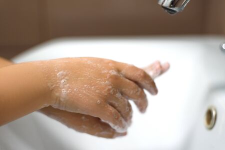 Washing of children's hands with soap under the crane with water.