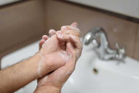 Washing of man's hands with soap under the crane with water.