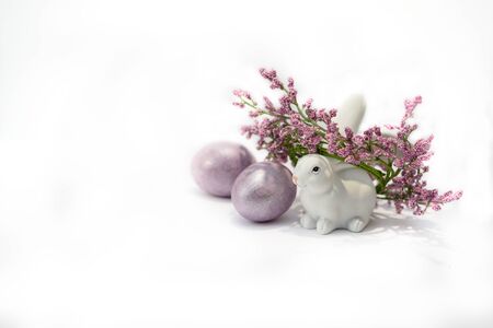 A white bunny rabbit with wreath of purple flowers and two colored easter eggs near. Easter holiday concept.の写真素材