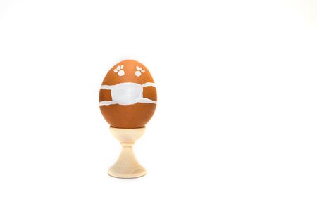 A brown chicken egg in mask in holder isolated on the white background. Coronavirus Covid-19....