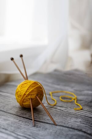 Yellow colored wool ball, knitting needles laying on the wooden background. Space for text.