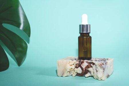 A glass dropper bottle on natural handmade soup on the green or mint background and litlle part of leaf of green monstera. Nature Skin concept. Organic Spa Cosmetics. Close up.の写真素材