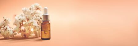 A glass dropper bottle with a pippette with white rubber tip and many beautiful white flowers near it on the orange background. Nature Skin concept. Organic Spa Cosmetics.の写真素材