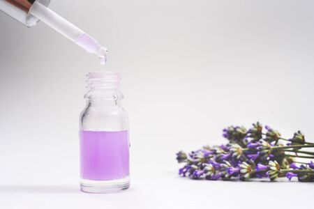 The pippette with white rubber tip from a glass dropper bottle with little drop of lavender oil and many beautiful lavender fresh flowers near it on the light grey background. Nature Skin concept. Organic Spa Cosmetics.の写真素材