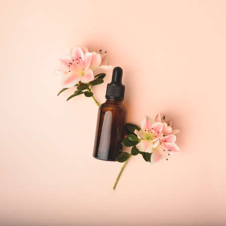 Serum glass bottle with pipette and beautiful flowers on the beige pink background. Natural Organic Spa Cosmetic concept. Front view.の写真素材