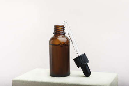 Opened glass dropper bottle with a pippette with black rubber tip on the beige background. Nature...