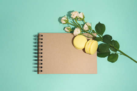 Flat lay of craft cketchbook with two yellow macarons and many beautiful beige roses on green...