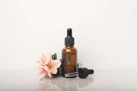 A glass dropper bottle with a pippette with black rubber tip and beautiful flower on grey...
