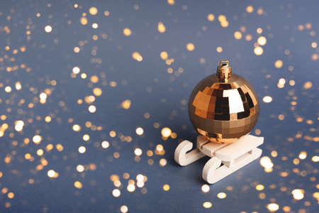 Golden christmas ball in sleds on the blue background with blurred sparkles.の写真素材