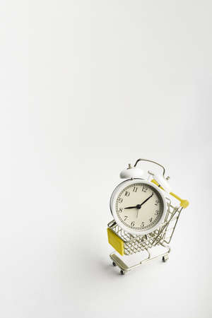 A supermarket trolley with old vintage alarm clock on white background. Shopping, purchases,...