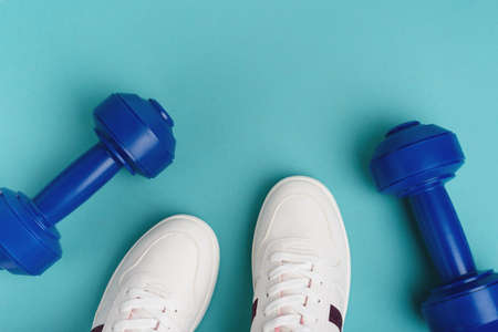White sport sneakers shoes and blue dumbbells on the blue background.の写真素材
