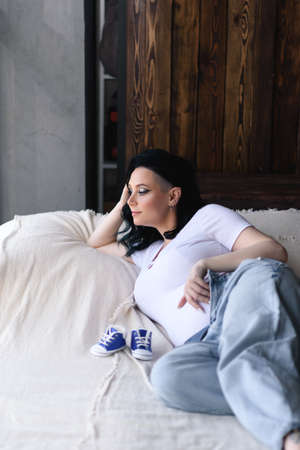 A pregnant woman on the bed wearing jeans and white T-shirt on wooden background.の写真素材