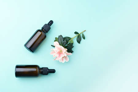 Serum glass bottles with pipette and beautiful flower on the green background. Natural Organic Spa...