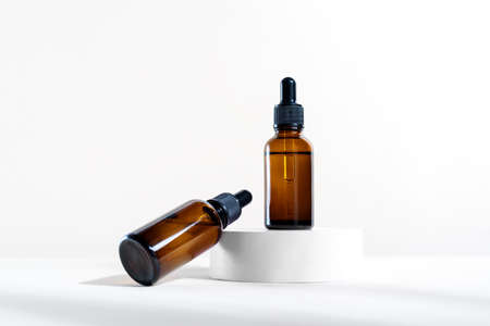 Glass dropper bottles with a pippette with black rubber tip on the white circle podium background. nature skin concept. Organic Spa Cosmetics. trendy concept.の写真素材