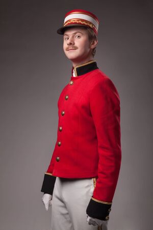 Portrait of a concierge  porter  in a red jacket on a gray background の写真素材