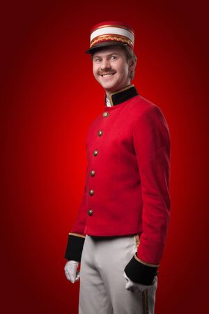 Portrait of a concierge  porter  in a red jacket on a red background の写真素材