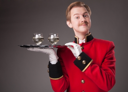 Smiling Waiter in red uniform with a tray with glasses on a grey backgroundの写真素材