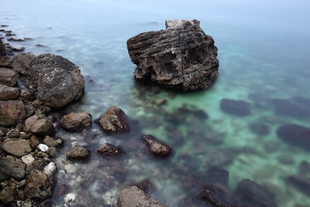 The sea with green transparent water, small stones on coast and a boulder at coast