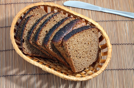 Cut black bread with caraway seeds in a wattled basket and a white knife lie on a mat