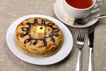 Breakfast in the form of pancakes with butter, a chocolate cream and a cup of tea 