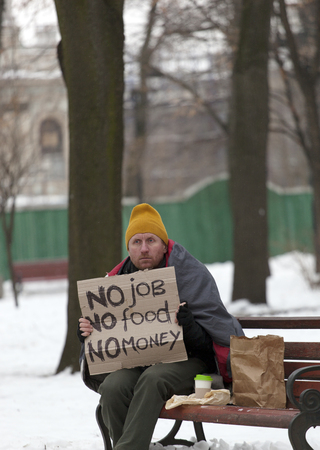 Adult sad homeless man with cardboard in winter city park