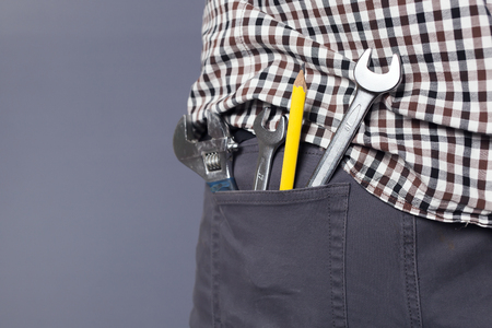 Wrenchs and toos, yellow pencil in a hip pocket of men's trousers on grey backgroundの写真素材