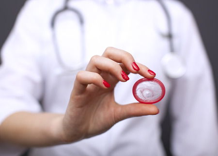 Red condom on palm of woman doctor. Close up.Conceptual image for health lifeの写真素材