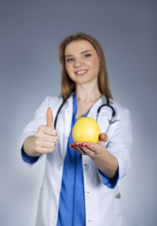 Young woman doctor holds on palm natural apple and finger up.の写真素材