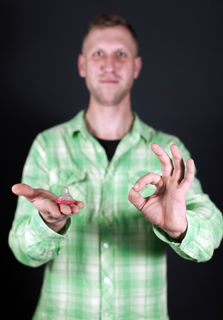 Red condom on palm of man in front of dark background. Sign OKの写真素材