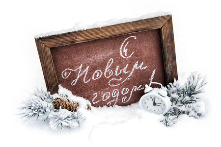 Happy New Year. A school board with a festive inscription, a cone, spruce branches and an alarm clock on the snowの写真素材