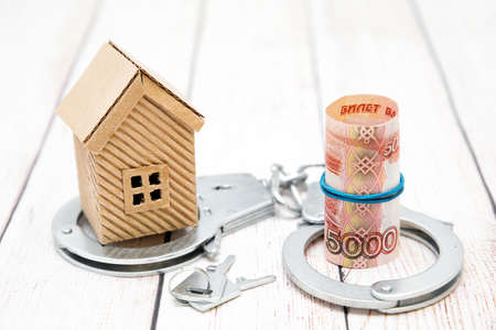 House, keys, money and handcuffs on the table. Fraud in the housing market