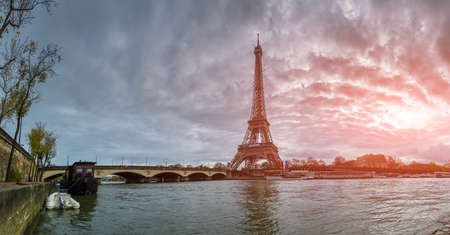 Beautiful panoramic view of the Eiffel Tower and Jena bridge from the river Seine embankment. Dramatic cloudscape. Traditional sitycape in backlit morning sunbeam. Paris, France.の写真素材