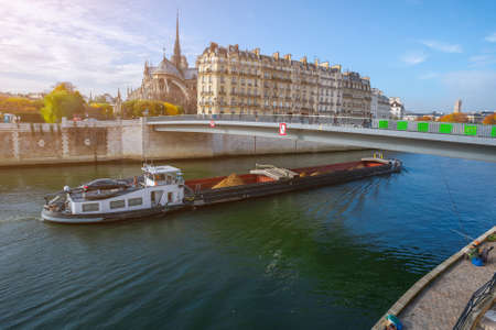 Cathedral of Notre Dame de Paris at autumn afternoon. Embankment of the Seine. Barge carrying a...