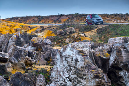 Small car on the side of the road. Picturesque landscape with weird rocks in a small canyon. Stormy...