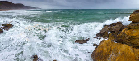 A huge ocean waves breaking on the coastal cliffs in at the cloudy stormy day. Breathtaking romantic panoramic seascape of ocean coastline. Peniche, Portugal.の写真素材