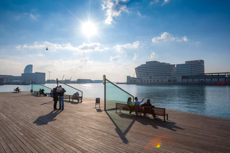 Spain, Barcelona - Dec 29, 2011: People Local and tourists have are rest and relaxing and walk in a leisurely way in a beautiful sunshine warm weather on a seafront Rambla De Mar near Maremagnum mall.のeditorial素材