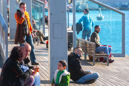Spain, Barcelona - Jan 01, 2012: People Local and tourists have are rest and relaxing and walk in a leisurely way in a beautiful sunshine warm weather on a seafront Rambla De Mar near Maremagnum mall.のeditorial素材