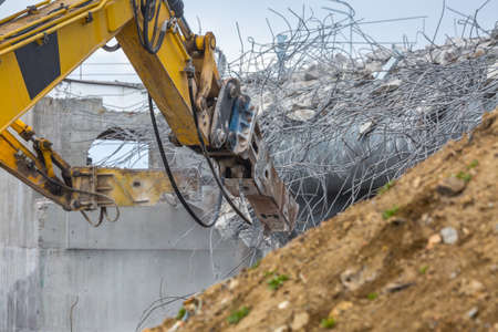 Professional demolition of reinforced concrete structures using industrial hydraulic hammer. Rods of metal fittings. Wreckage and crumbles of concrete.の写真素材